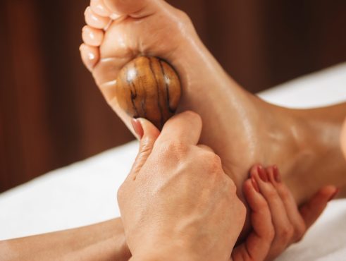 Reflexology - foot massage with rounded wooden massage tool. Reflexologist applying pressure to client’s foot